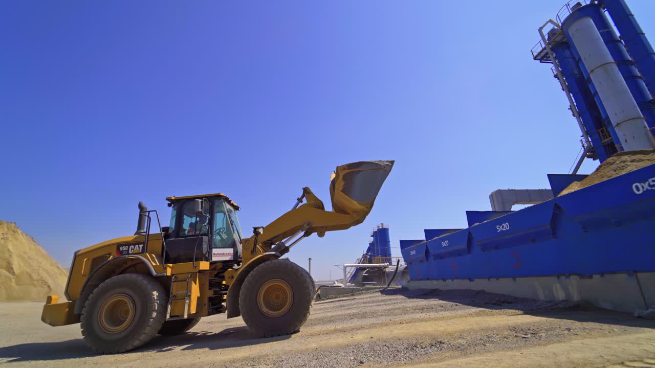 Contemporary asphalt factory background. Excavator transports asphalt into special tanks outdoors.