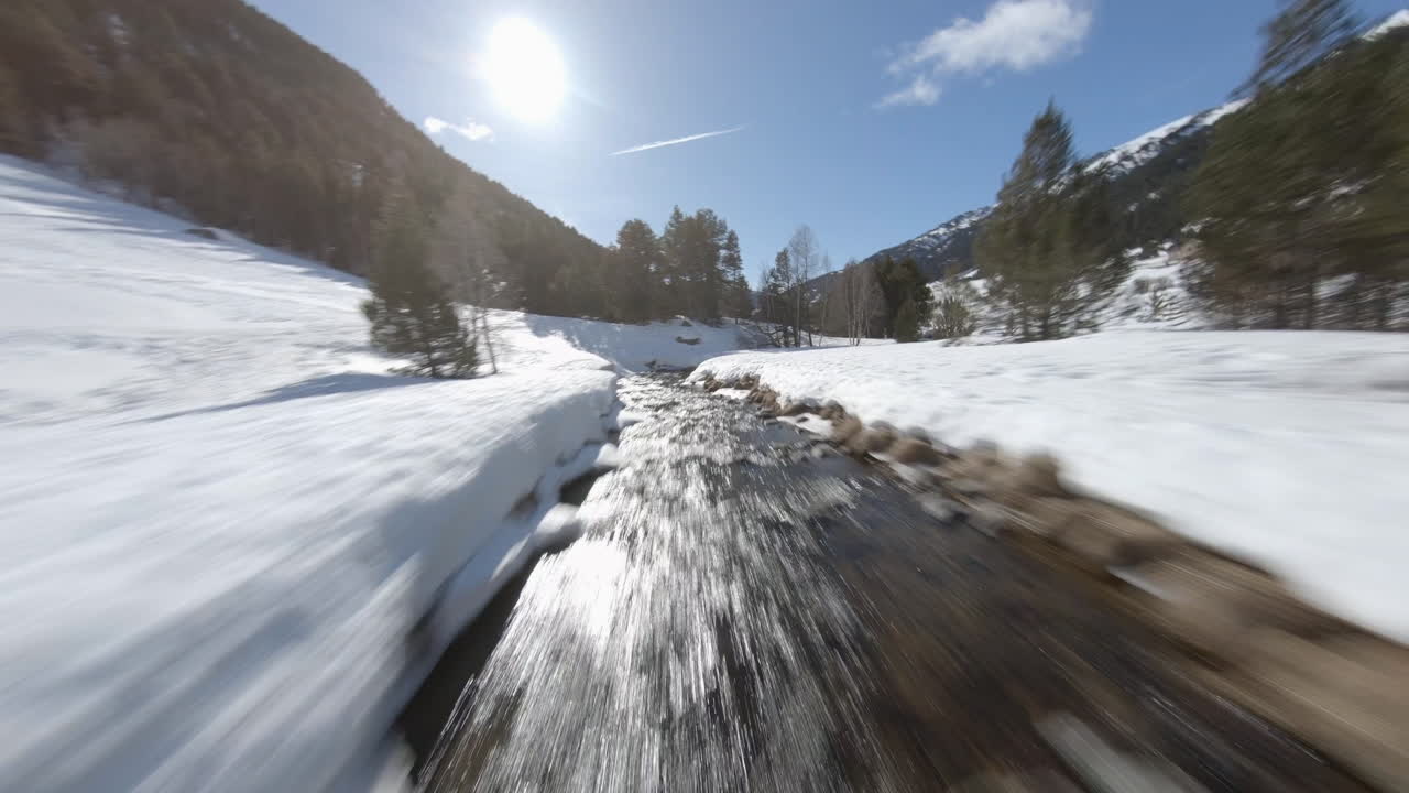 Aerial drone fpv over stream flowing on snowy and frozen Incles valley on sunny day, Pyrenees