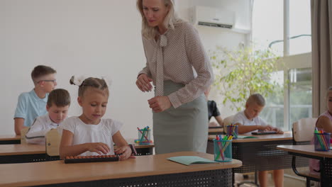 female teacher controlling learning process in primary school. a female teacher walks between the desks and looks after the completion of the task