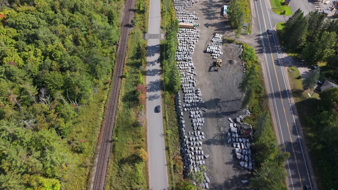 A top-down drone shot over Gravenhurst showing parallel roads, a railway, a stone supply yard, vehicles passing, and surrounding trees