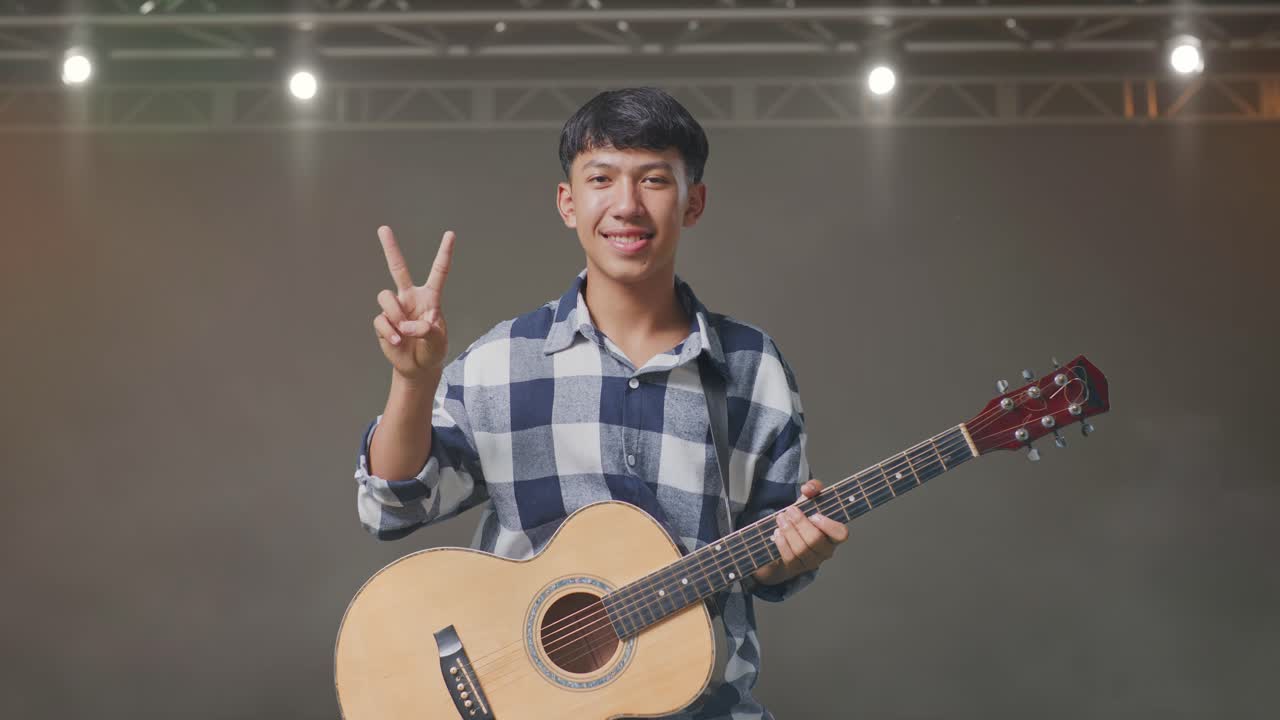 기타를 들고 있는 아시아인 십대가 무대에서 평화와 미소를 짓고 있습니다.