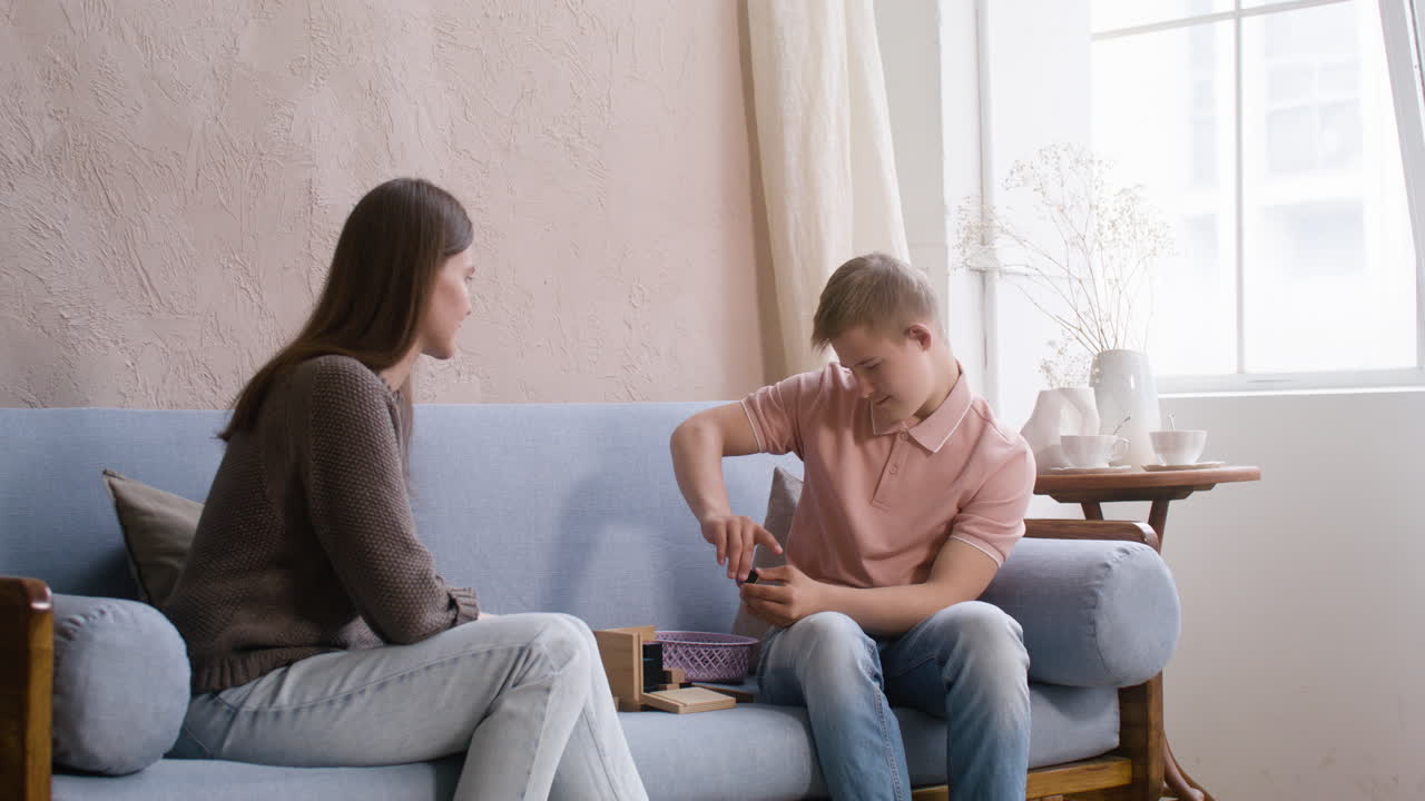 En dreng med Downs syndrom og hans mor leger med trækuber på sofaen i stuen derhjemme.