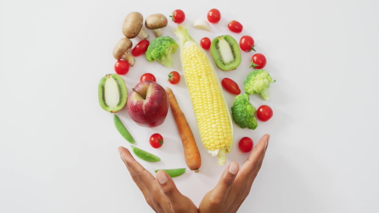 Video of biracial man's hands and fresh fruit and vegetables on white background
