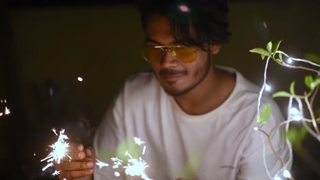 joven asiático feliz celebra la navidad, el diwali o la fiesta de año nuevo jugando con fuegos artificiales y petardos junto a las luces decoradas en la planta