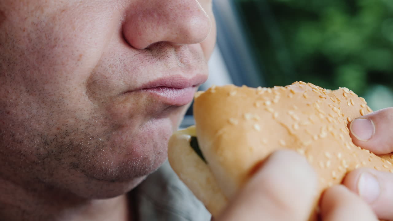 un hombre hambriento come ansiosamente una hamburguesa solo su boca es visible en el marco