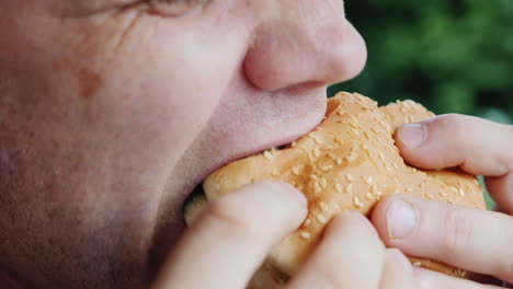 a hungry man eagerly eats a hamburger only his mouth is visible in the frame