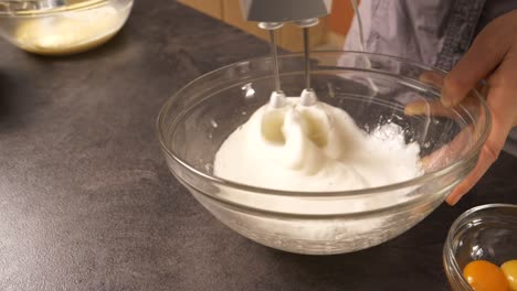 a close-up shot of a young woman using an electric mixer beating the egg white to create foam for a cake filling