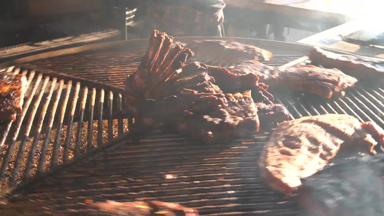 Chef che gira deliziose costine e carne su un barbecue fumante all'aperto