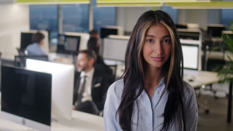 front view of beautiful young woman professional wearing blue shirt. portrait of young female office manager looking to camera and having good mood. blurred office background