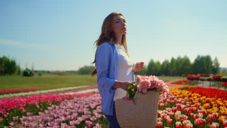 relaxed woman with basket of flowers standing in beautiful blooming tulip field.