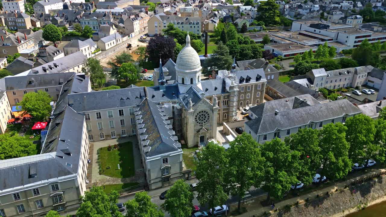 Drone slowly rotates around Saint Julien Chapel, showing Mayenne riverbanks and Laval cityscape on a clear day.