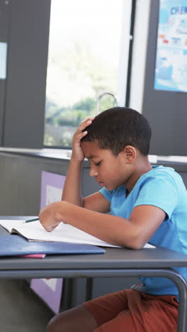 vertical video: in school, child studying and writing in notebook, concentrating on work