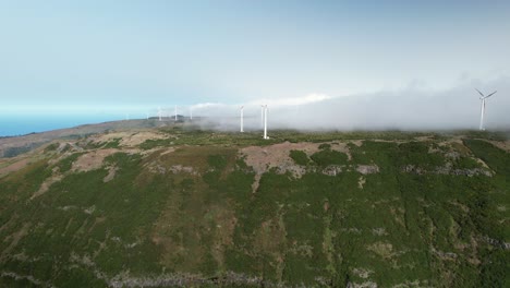 el avión no tripulado vuela hacia las turbinas eólicas giratorias cubiertas de nubes en la cima de la colina de madeira