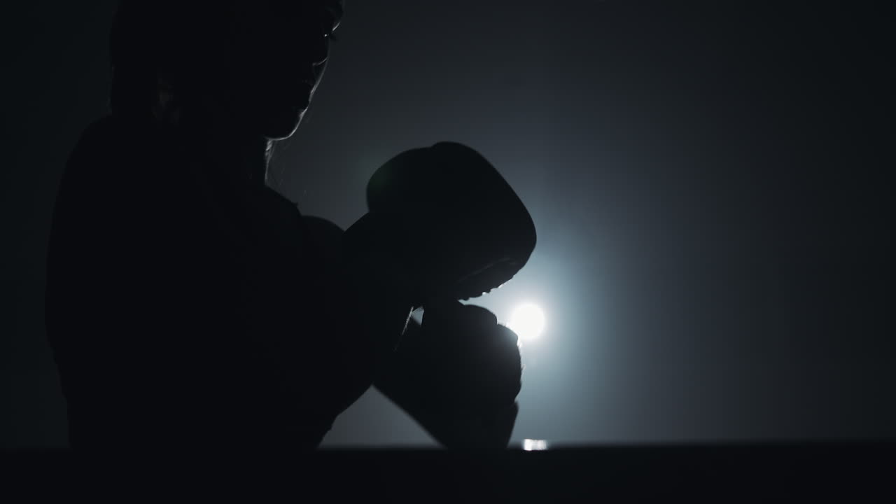 Silhouette di un pugile che si allena in una palestra buia