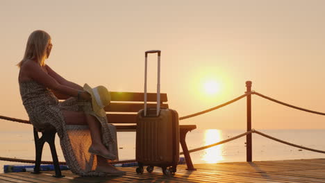 the girl is waiting for settling into the hotel on the sea pier sits along with suitcases and enjoys