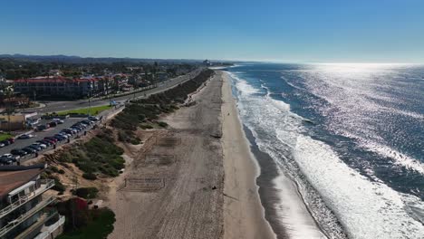 aerial drone shot over the sandy beach of carlsbad, california, usa and the pacific coast highway passing by beside the beach on a townscape