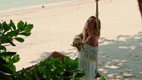woman enjoying a coconut on a beach swing
