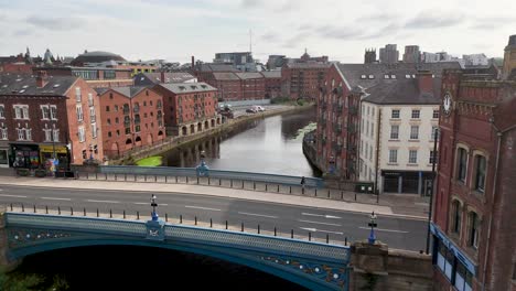 aerial camera smoothly pans over leeds city center, revealing victorian brick buildings, river aire, and a bridge under soft daylight with overcast skies