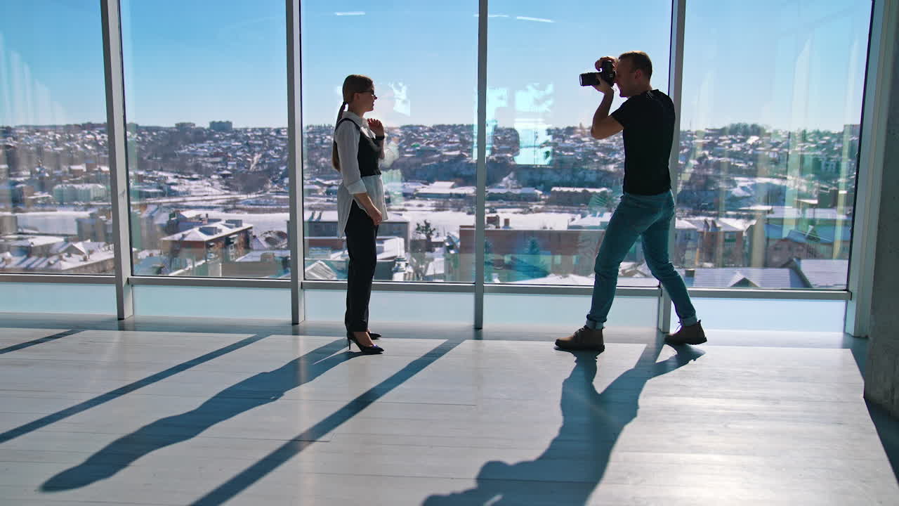 Business woman posing on camera near office window. Young photographer taking photos of a beautiful woman in business clothes on the background of windows.