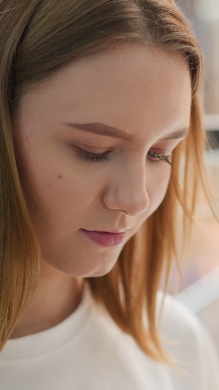 Young woman focuses intently, appearing thoughtful and absorbed, with soft lighting and blurred background in modern mall environment