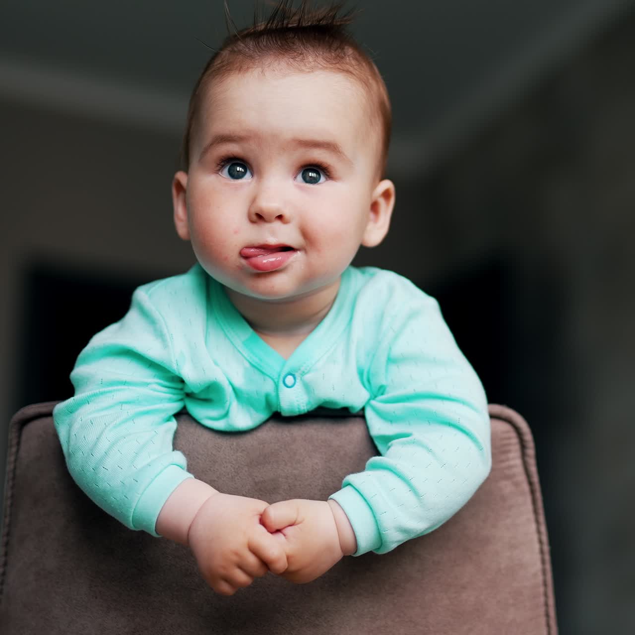 Sweetheart baby stands leaning on chair back. Cute kid stares in front of him. Low angle view