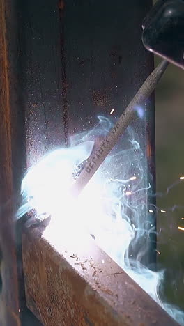 closeup skilled craftsman fixes metal detail to country house fence pole using welding tool outdoors