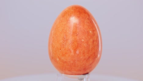 orange marble egg rotating slowly on a turntable in front of a white background