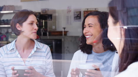 female friends laughing at coffee shop, seen through window