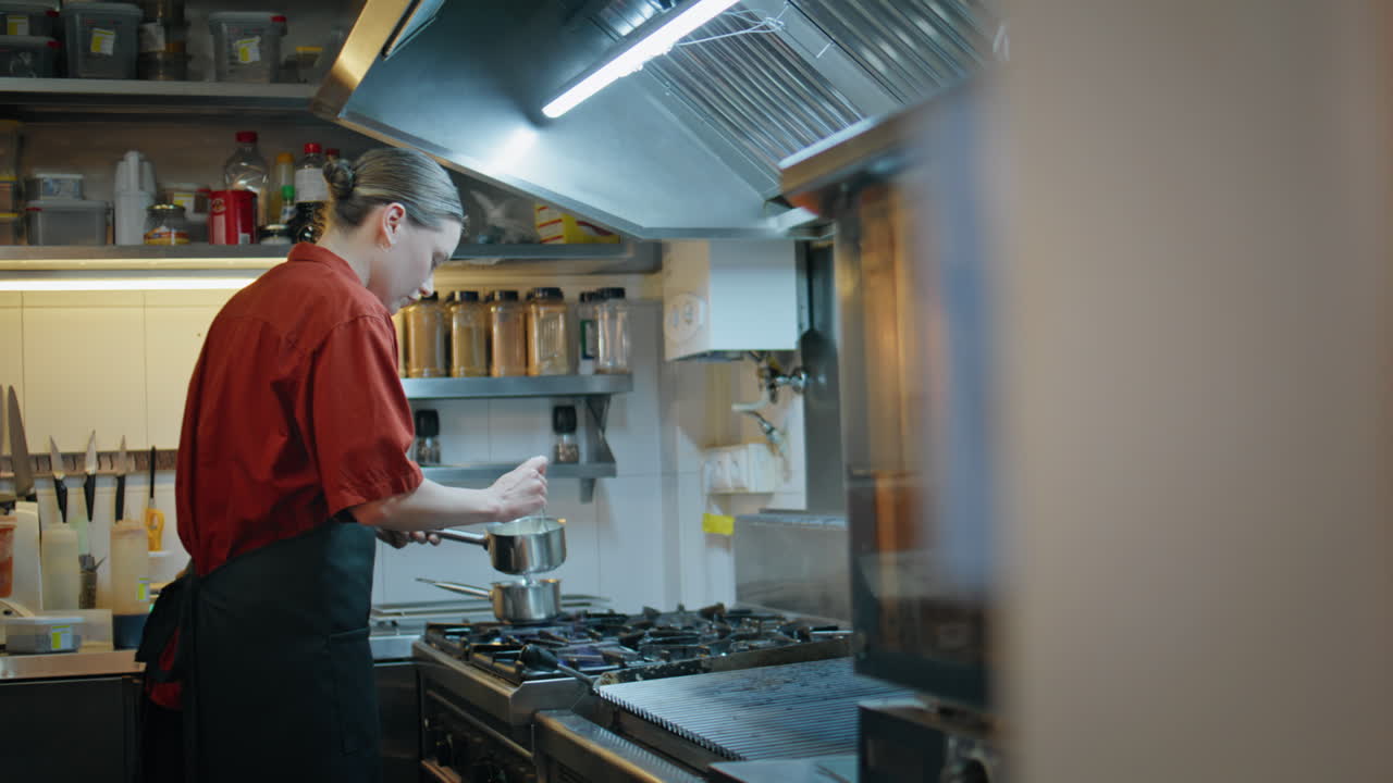 Kitchen worker preparing sauce in pan modern restaurant. Woman chef cooking