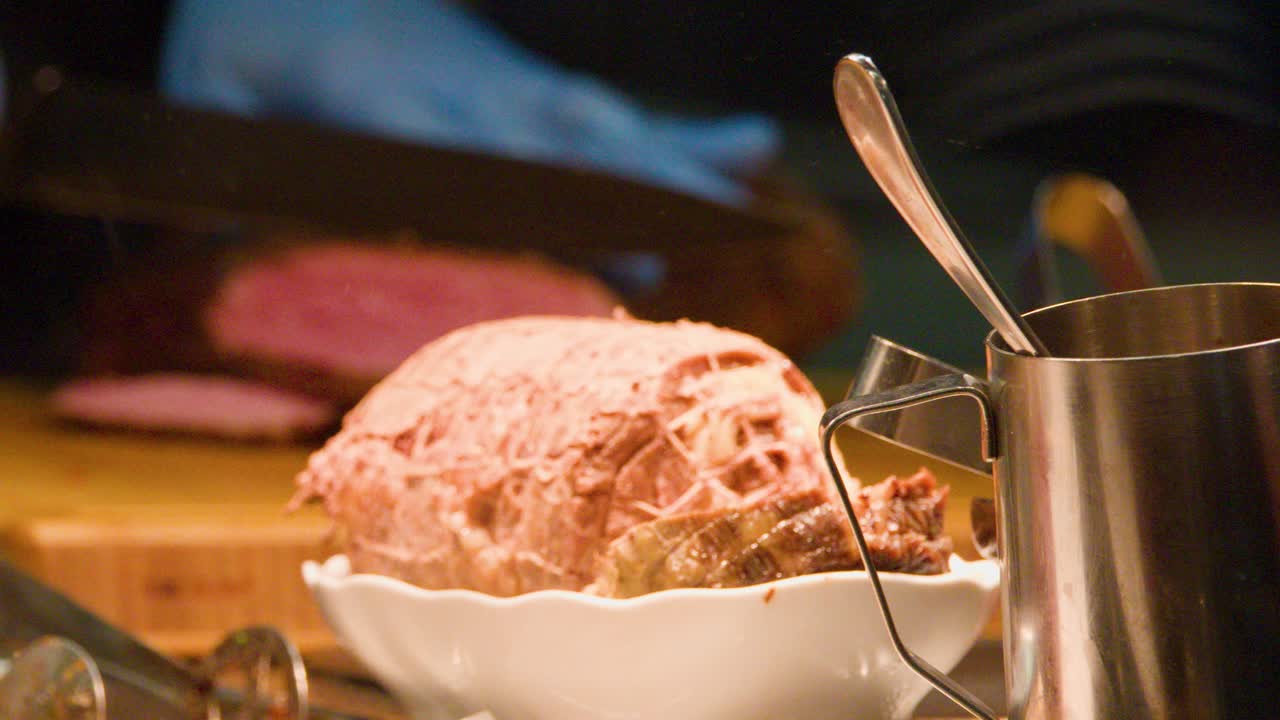 Uno chef con i guanti taglia roast beef su un tagliere di legno sotto una luce calda nella cucina di un mercato di Praga