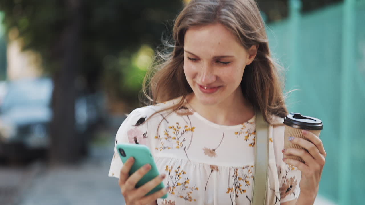 Happy Young Woman Walking and Using Smartphone with Coffee