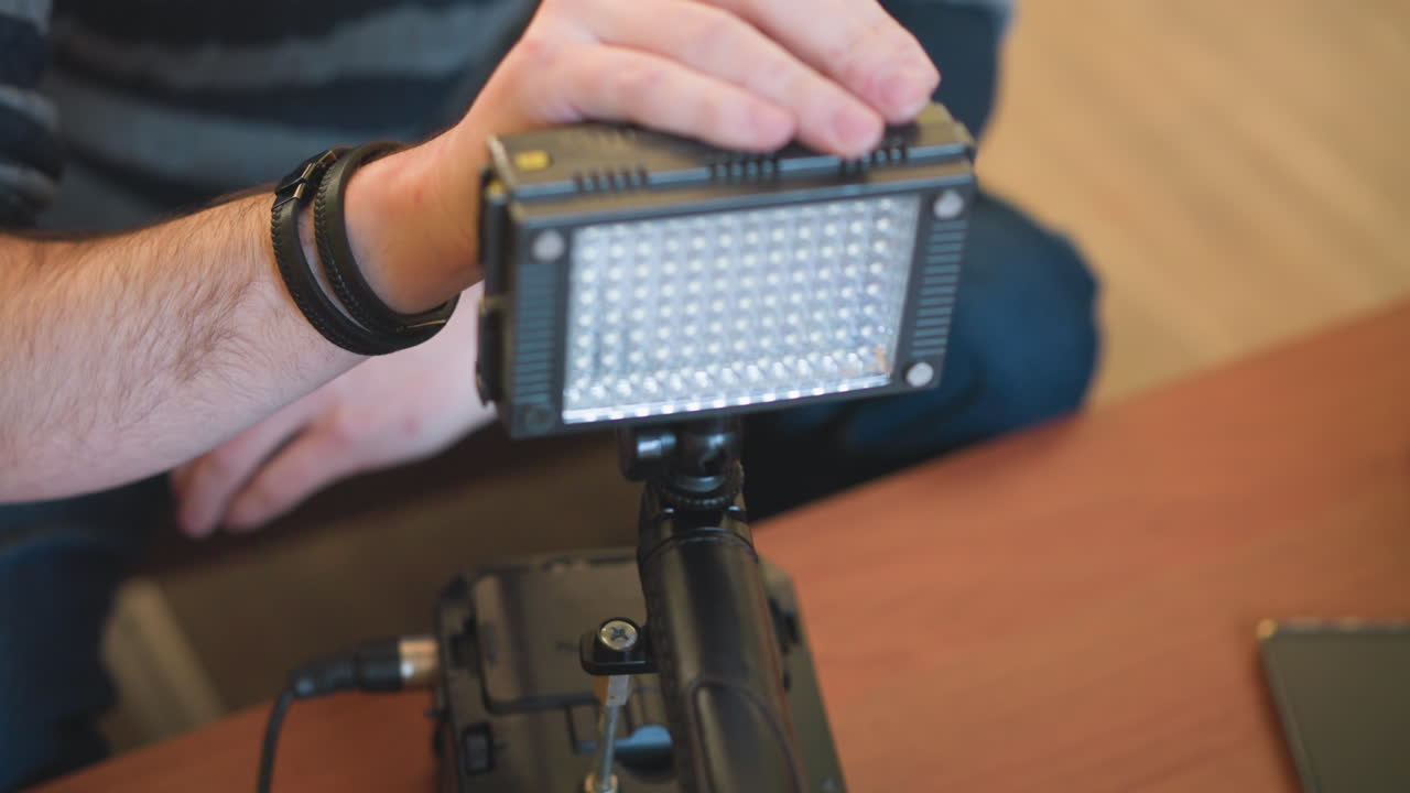 Studio guy adjusting light panel while setting up video equipment. Focus on hands handling light attachment, background blurred. Studio scene with professional gear and lighting setup