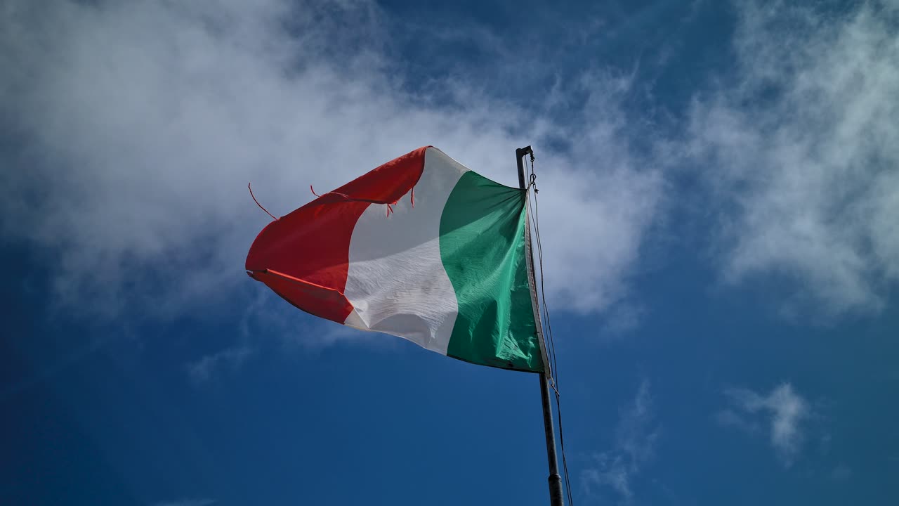 Bandiera Italiana che sventola su asta sotto il cielo estivo, inquadratura dal basso.