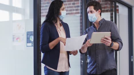 Man-and-woman-wearing-face-masks-discussing-at-office