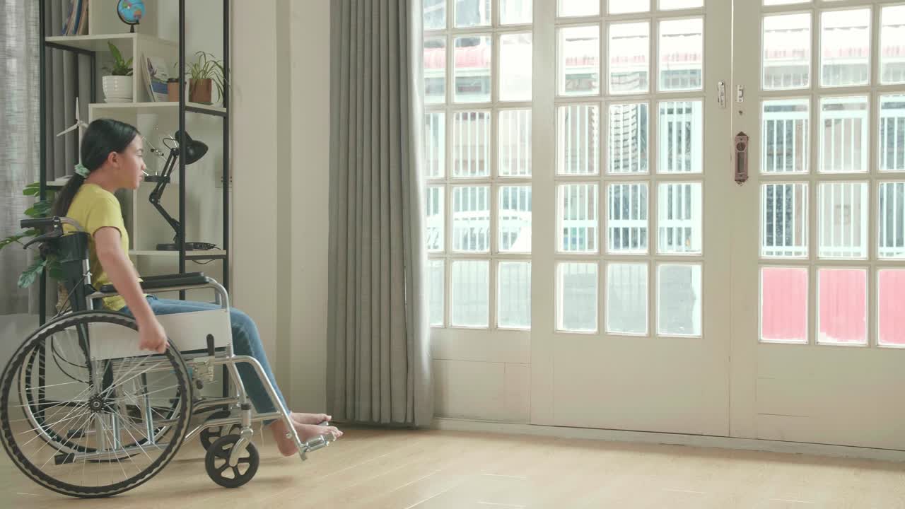 Asian Kid Girl Sitting In A Wheelchair Looking Out Of A Door