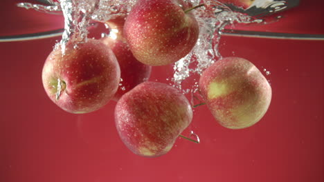 cámara lenta de manzanas orgánicas frescas cayendo al agua sobre fondo rojo