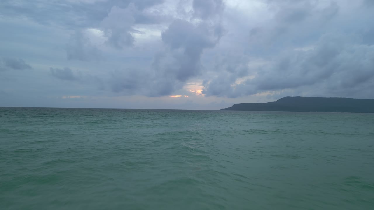 Camera moves over a windy beach out towards a vast ocean beneath a cloudy sky.