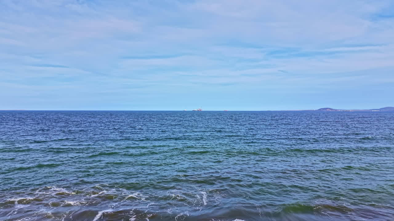 Vista di onde oceaniche sotto un cielo nuvoloso, con terraferma in lontananza osservata in una giornata limpida vicino alla costa.