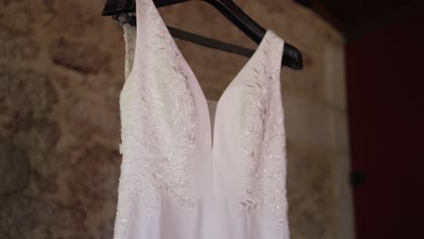 close up of a wedding dress with intricate lace detailing, hanging against a rustic stone wall