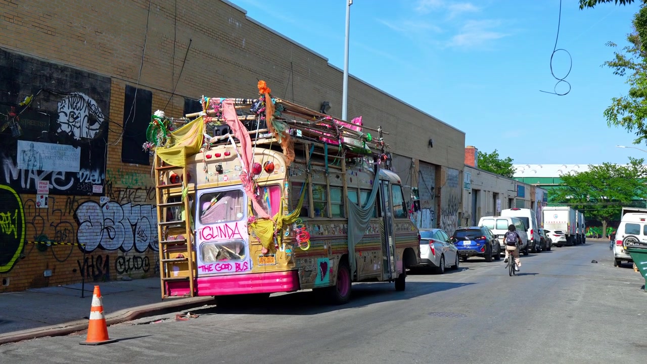 New York, États-Unis, 5 juin 2026 : Bus décoré et cycliste dans une rue industrielle couverte de graffitis. Échelle arrière, auvent en tissu, fourgonnettes de livraison.