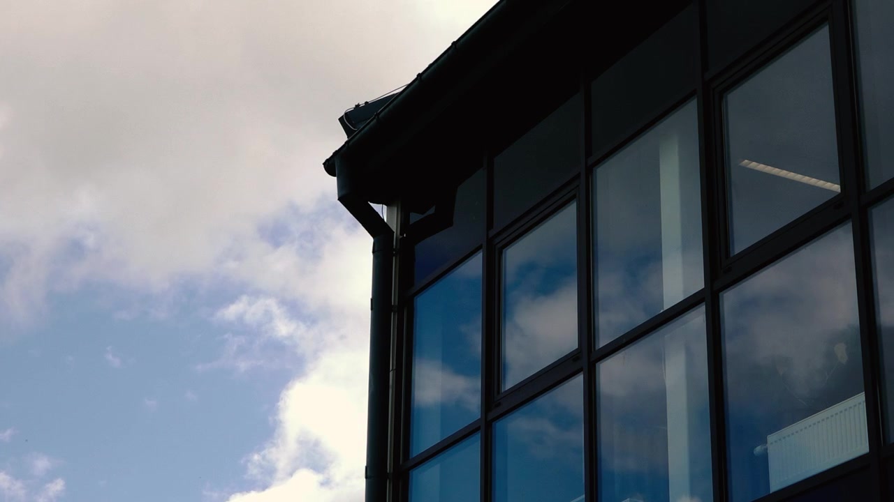 Finestre di un edificio moderno riflettono cielo blu e nuvole accanto a cielo aperto con luce soffusa, architettura geometrica