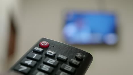 Hand-closeup-of-the-man-with-the-remote-control-and-watching-the-television-with-presses-to-change-the-channel-on-the-button