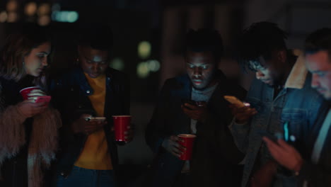 group of friends relaxing on rooftop at night using smartphone technology texting sharing social media lifestyle browsing online enjoying weekend party