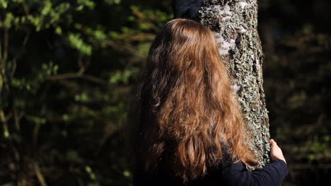 mujer con cabello castaño largo abrazando a un árbol, mirando hacia arriba sonriendo