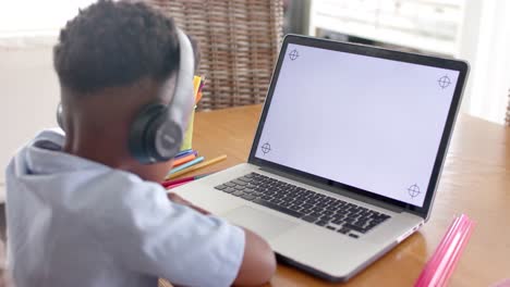 african american boy in headphones using laptop in online class at home, slow motion, copy space