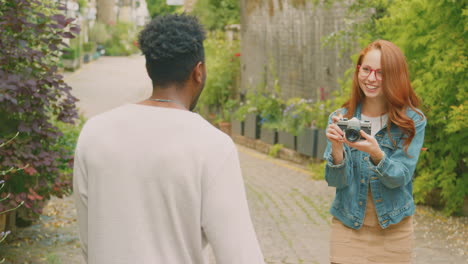 man posing and woman taking photos on camera as young couple travel through city together