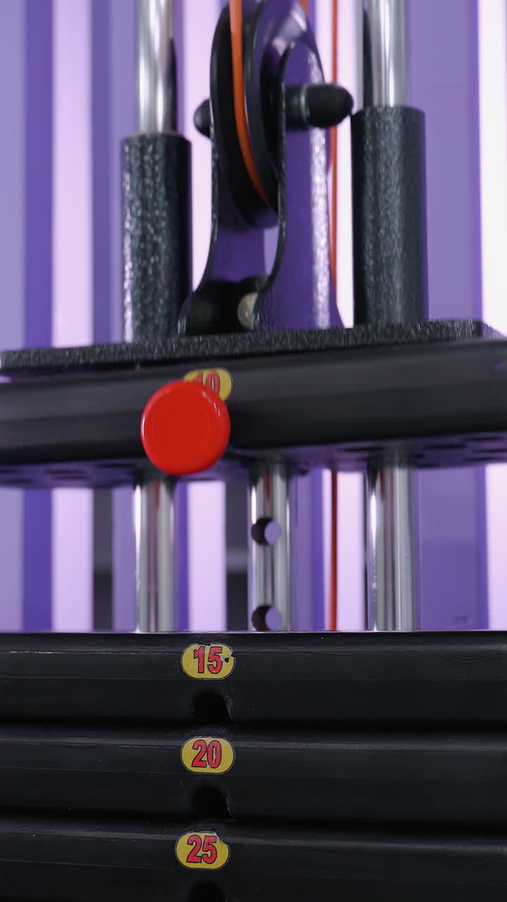 Weight stack drops gradually on a gym resistance machine, displaying labeled plates for adjustable strength training, the smooth motion emphasizes controlled exercise