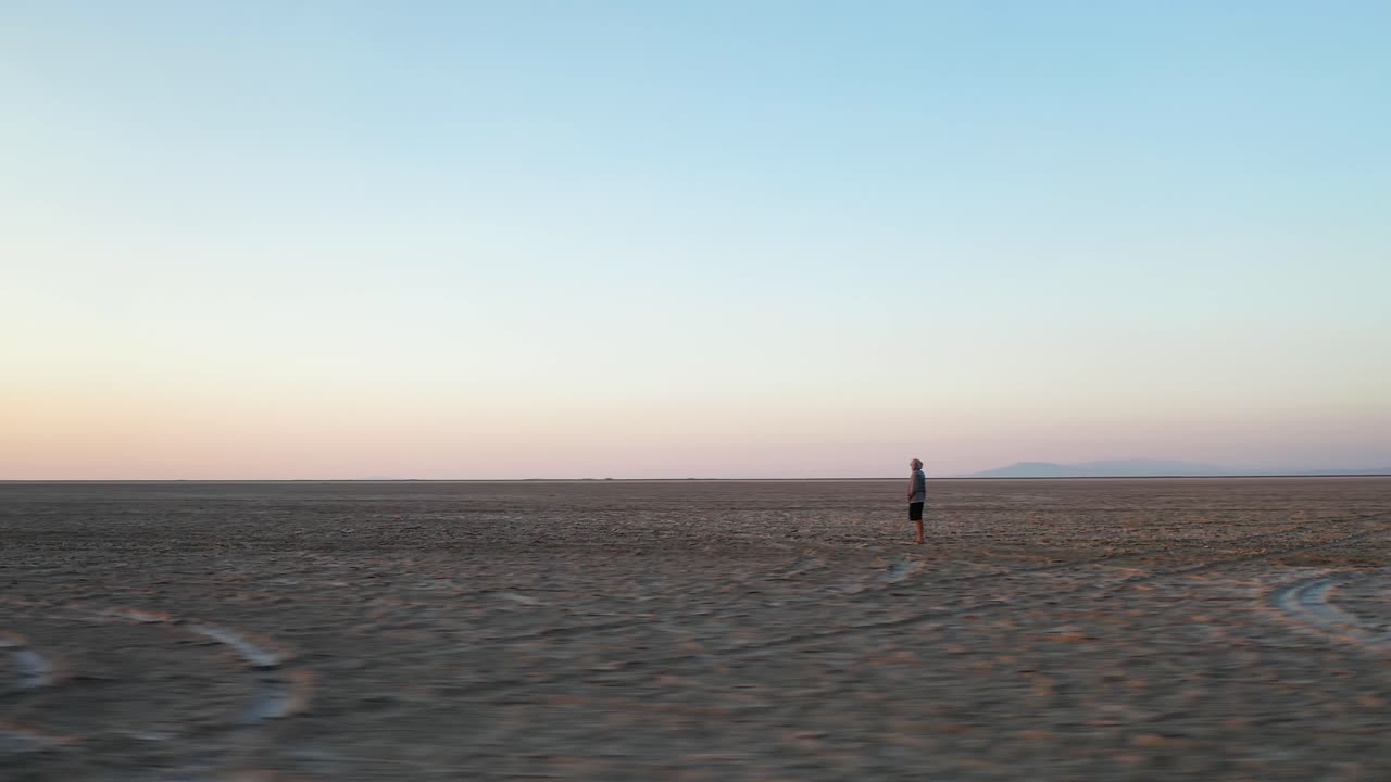 Orbit Aerial View of a Lonely Man Standing in Endless Desert Landscape Watching Sunrise