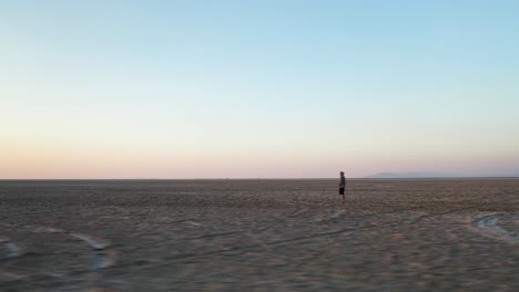 Orbit-Aerial-View-of-a-Lonely-Man-Standing-in-Endless-Desert-Landscape-Watching-Sunrise