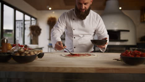 man cooking italian pizza in restaurant. chef spreading tomato sauce in kitchen.